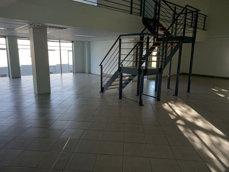 Spacious open-plan office area featuring tiled flooring, a modern metal staircase, and large windows providing ample natural light.