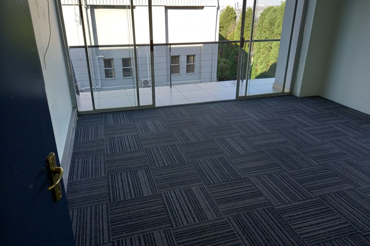 Empty office space featuring modern carpet tiles and large sliding glass doors leading to a private balcony with exterior views.