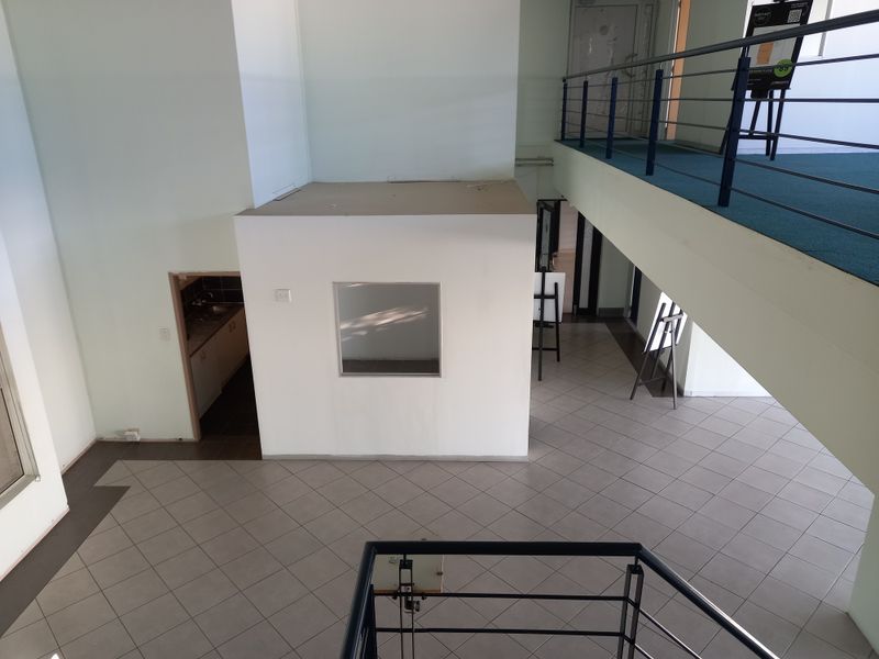 Spacious open-plan office interior featuring a mezzanine level, tiled flooring, and a dedicated kitchenette area with a modern, airy layout.