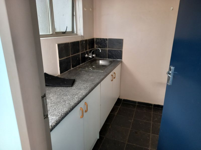 A compact kitchenette featuring a stainless steel sink, laminate countertop, and tiled splashback, suitable for a small office utility area.