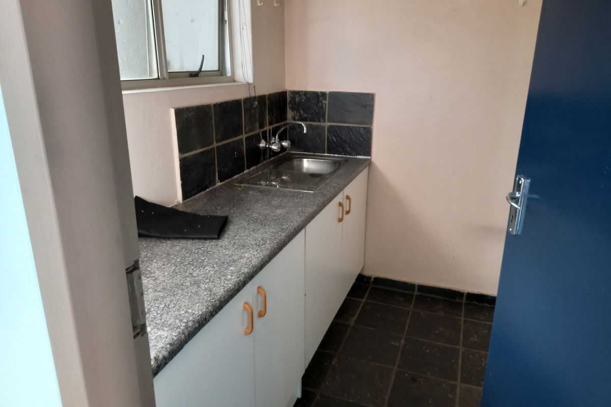 A compact kitchenette featuring a stainless steel sink, laminate countertop, and tiled splashback, suitable for a small office utility area.