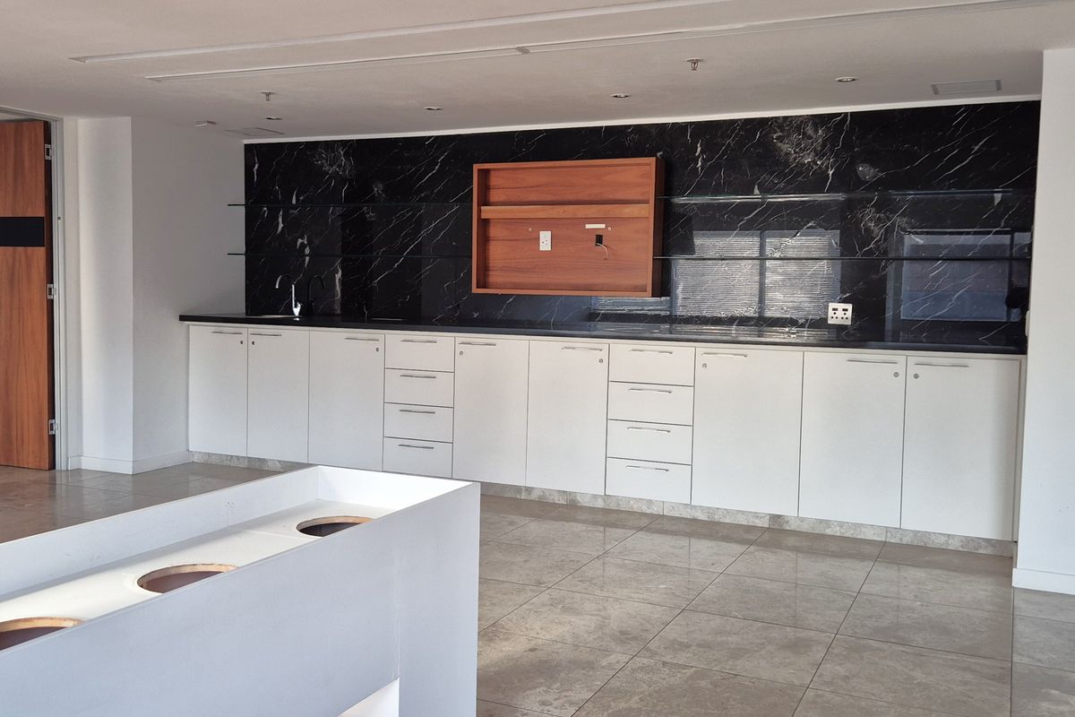 A modern office kitchenette featuring white cabinetry, a black marble-style backsplash, and a central island unit with integrated circular cutouts.