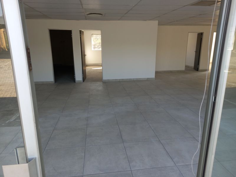 An empty, open-plan office space featuring neutral tiled flooring, a suspended ceiling, and multiple internal doorways leading to separate rooms.