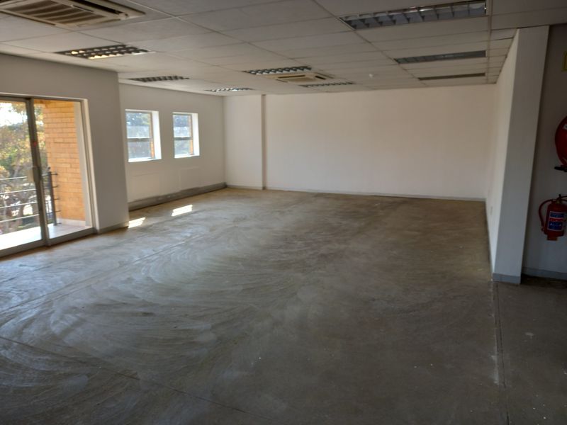 An empty, open-plan office space featuring a suspended ceiling, recessed lighting, ducted air conditioning, and access to a balcony through sliding glass doors.