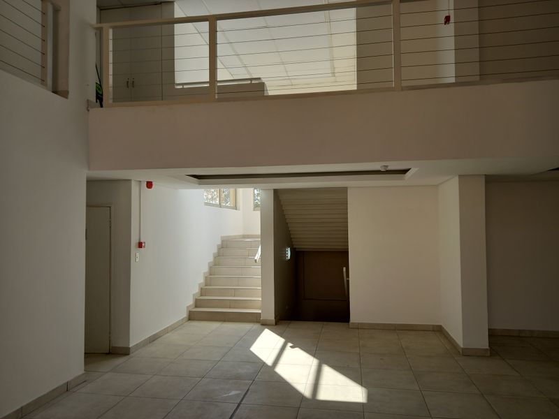 Spacious office entrance area featuring tiled flooring, a central staircase, and a mezzanine level with a modern metal balustrade.