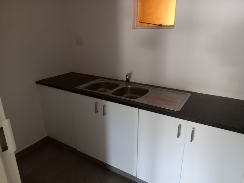 A clean, functional kitchenette area featuring white base cabinetry, a dark laminate countertop, and a double bowl stainless steel sink.