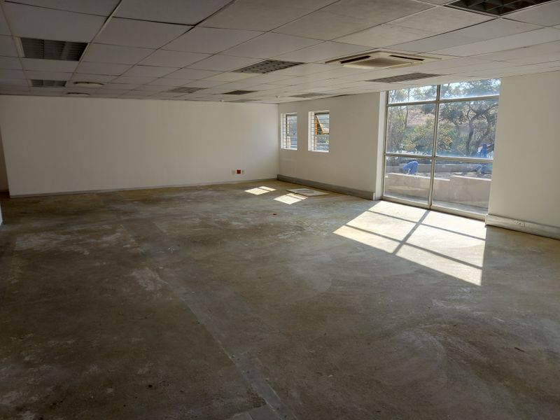 Spacious, empty office area featuring a suspended ceiling with integrated air conditioning and large windows providing ample natural light.