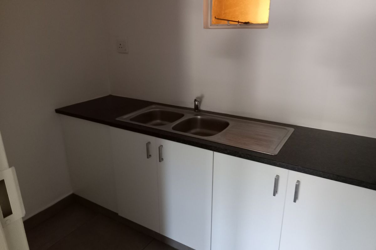 A clean, functional kitchenette area featuring white base cabinetry, a dark laminate countertop, and a double bowl stainless steel sink.