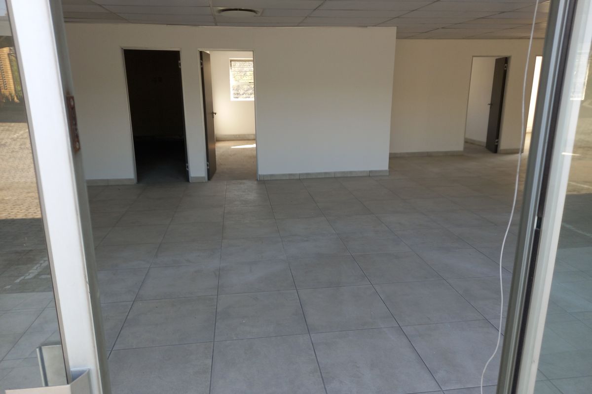 An empty, open-plan office space featuring neutral tiled flooring, a suspended ceiling, and multiple internal doorways leading to separate rooms.