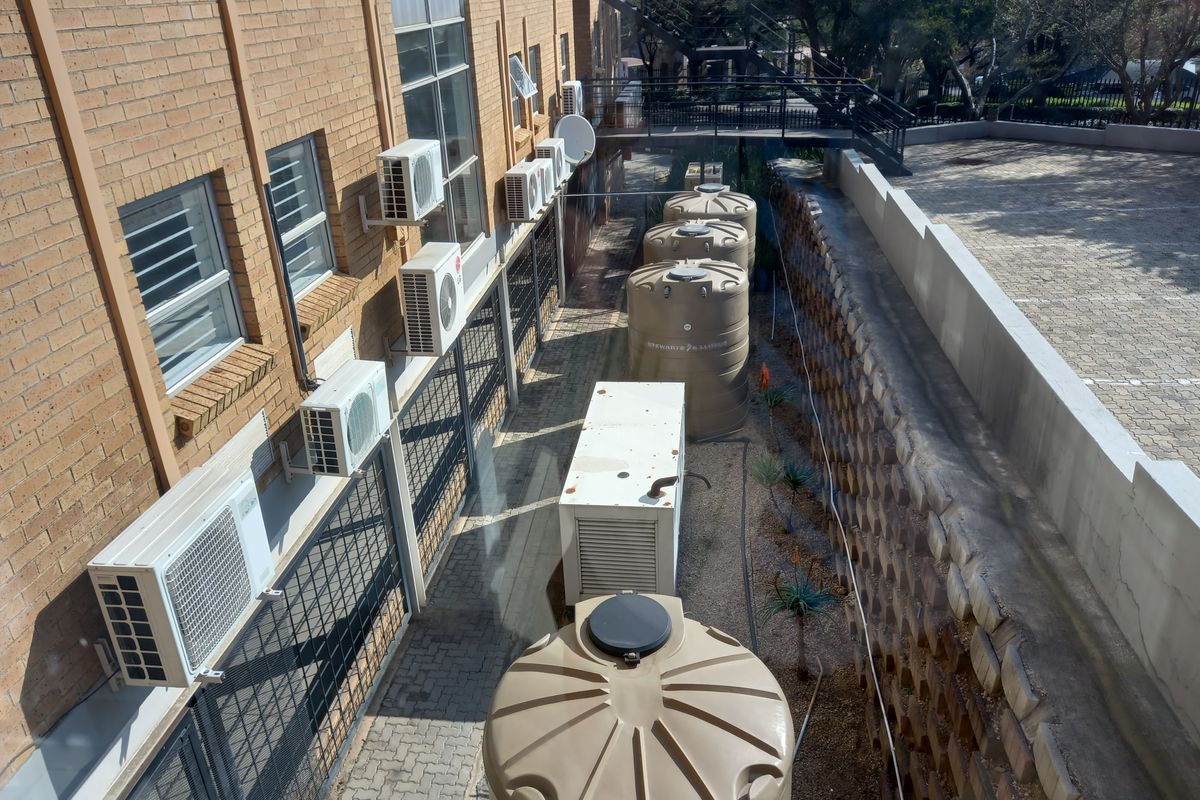 Rear exterior view of the office building featuring multiple air conditioning units, water storage tanks, a generator enclosure, and a paved service area.