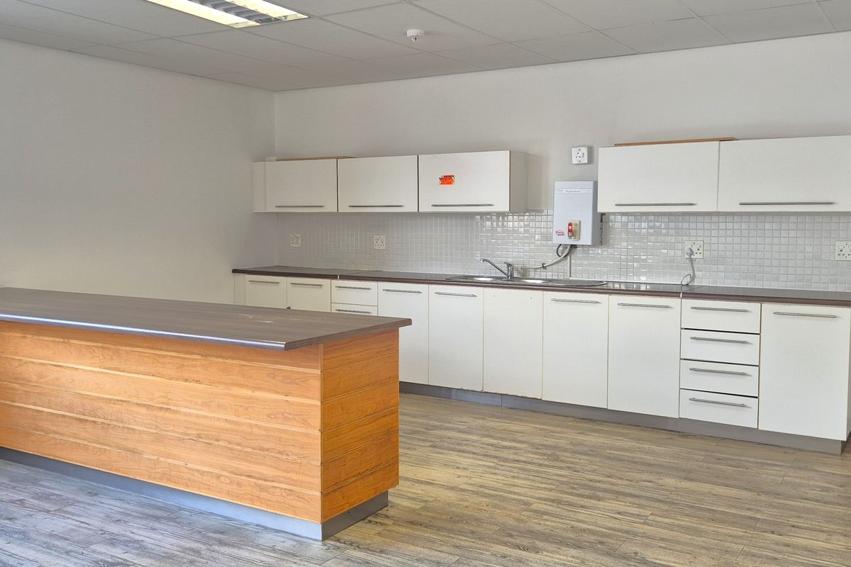 A functional office kitchenette featuring white cabinetry, a tiled backsplash, a stainless steel sink, and a wooden breakfast bar counter.