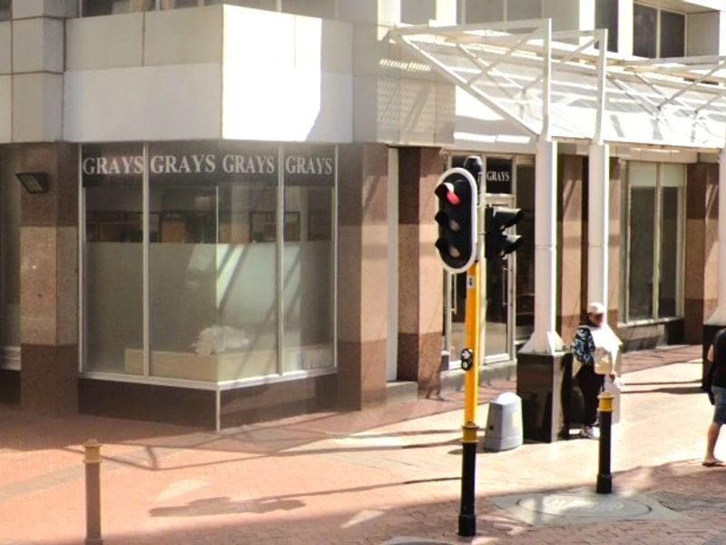 Street-level view of a retail storefront featuring large display windows, stone cladding, and a covered pedestrian walkway.