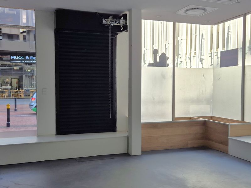 Bright retail entry space featuring large glass storefront windows, built-in bench seating, and a secure roller shutter mechanism.