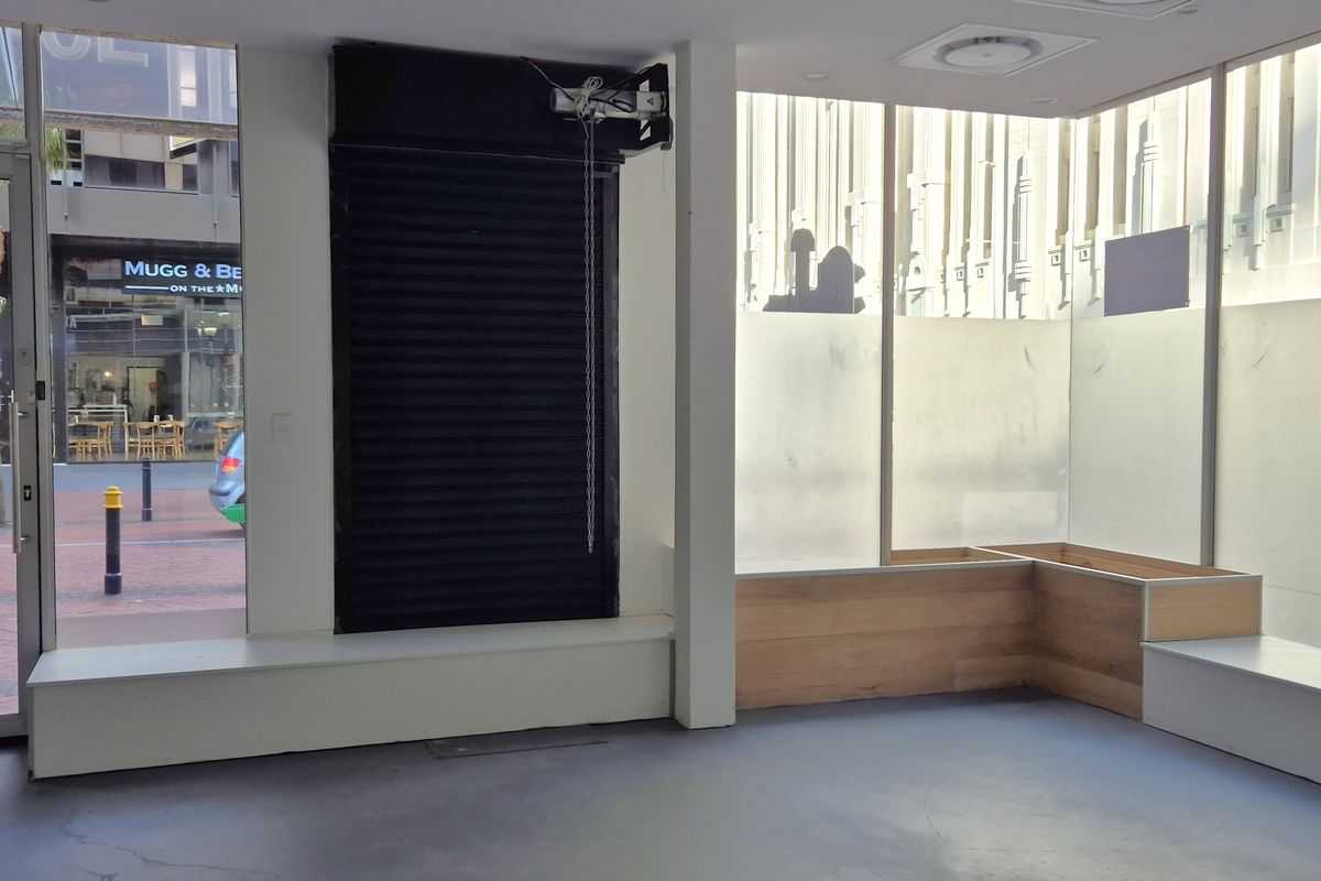 Bright retail entry space featuring large glass storefront windows, built-in bench seating, and a secure roller shutter mechanism.
