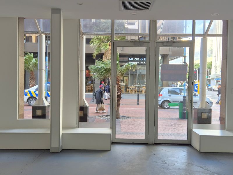 Empty retail storefront featuring large glass windows, double entry doors, built-in display platforms, and a secure black metal roller shutter.