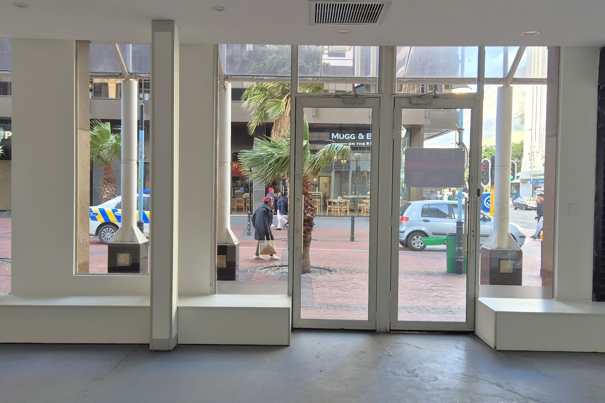 Empty retail storefront featuring large glass windows, double entry doors, built-in display platforms, and a secure black metal roller shutter.