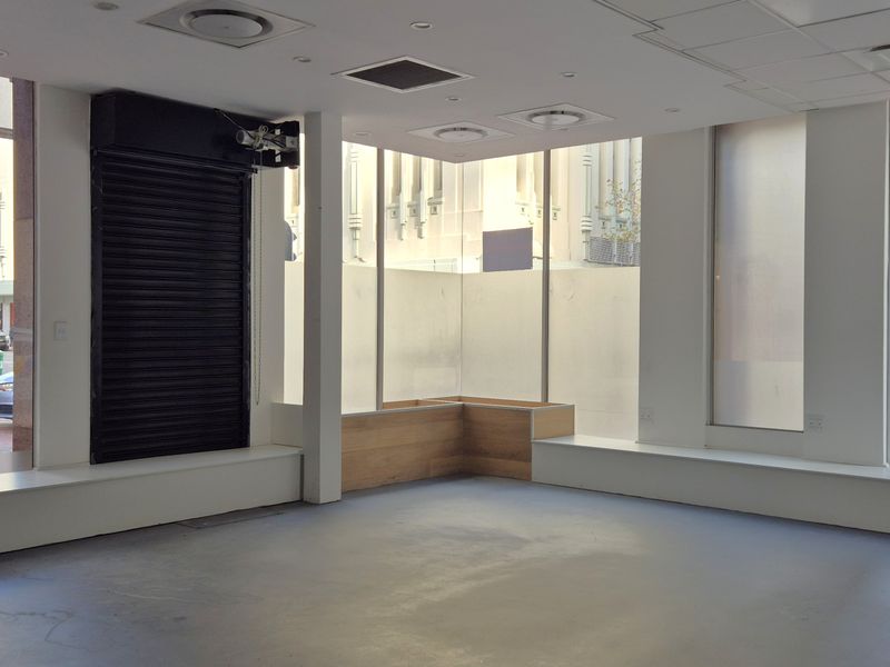 Bright open-plan retail space featuring large display windows, built-in bench seating, recessed lighting, and durable concrete flooring in a high-visibility street-level location.