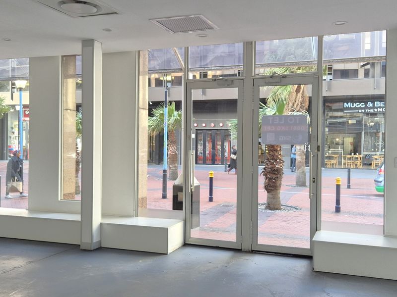Empty retail storefront featuring large glass windows, double entry doors, and built-in display plinths, offering excellent visibility in a busy pedestrian area.