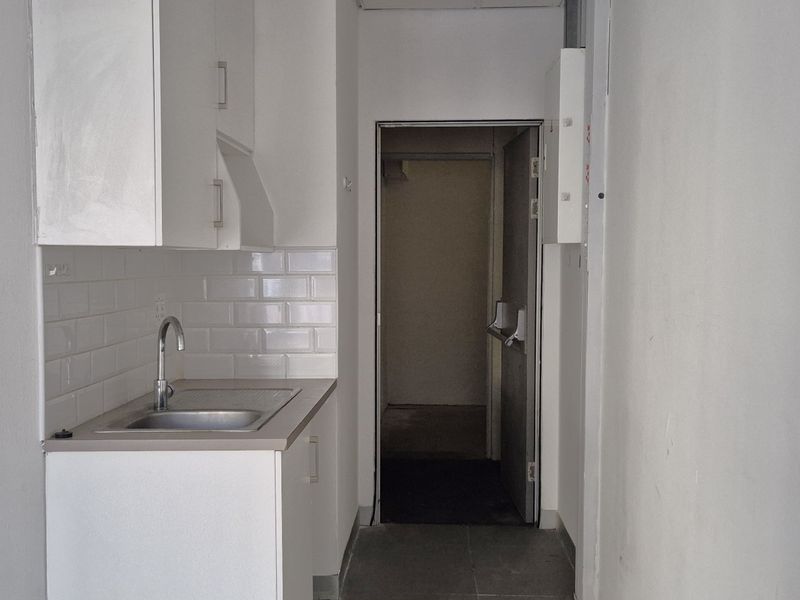 A compact kitchenette featuring white cabinetry, a stainless steel sink, and a subway tile backsplash, leading into an adjacent utility area.