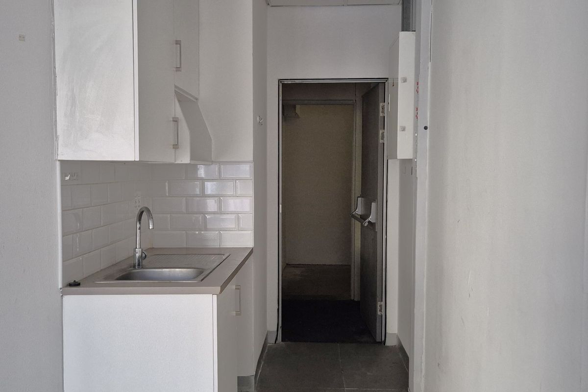 A compact kitchenette featuring white cabinetry, a stainless steel sink, and a subway tile backsplash, leading into an adjacent utility area.