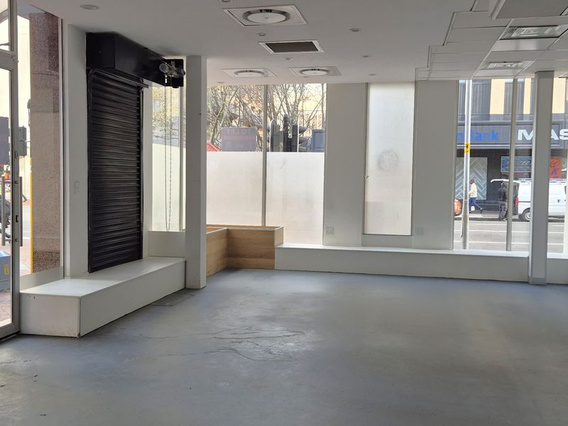 Vacant retail space featuring large street-facing display windows, built-in platforms, recessed lighting, and a secure entrance, suitable for various commercial uses.