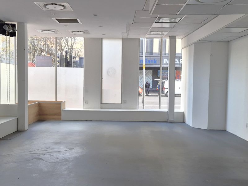 A vacant, open-plan retail space featuring large display windows, a suspended ceiling with recessed lighting, and durable concrete flooring, ideal for a showroom or shop.