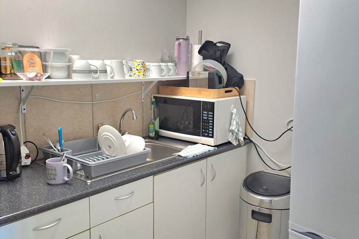 A compact office kitchenette featuring laminate countertops, stainless steel sink, built-in cabinetry, and a dedicated space for a refrigerator.