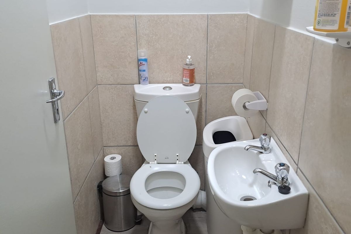 A compact office restroom featuring a standard toilet, wall-mounted basin, and neutral ceramic wall tiling.
