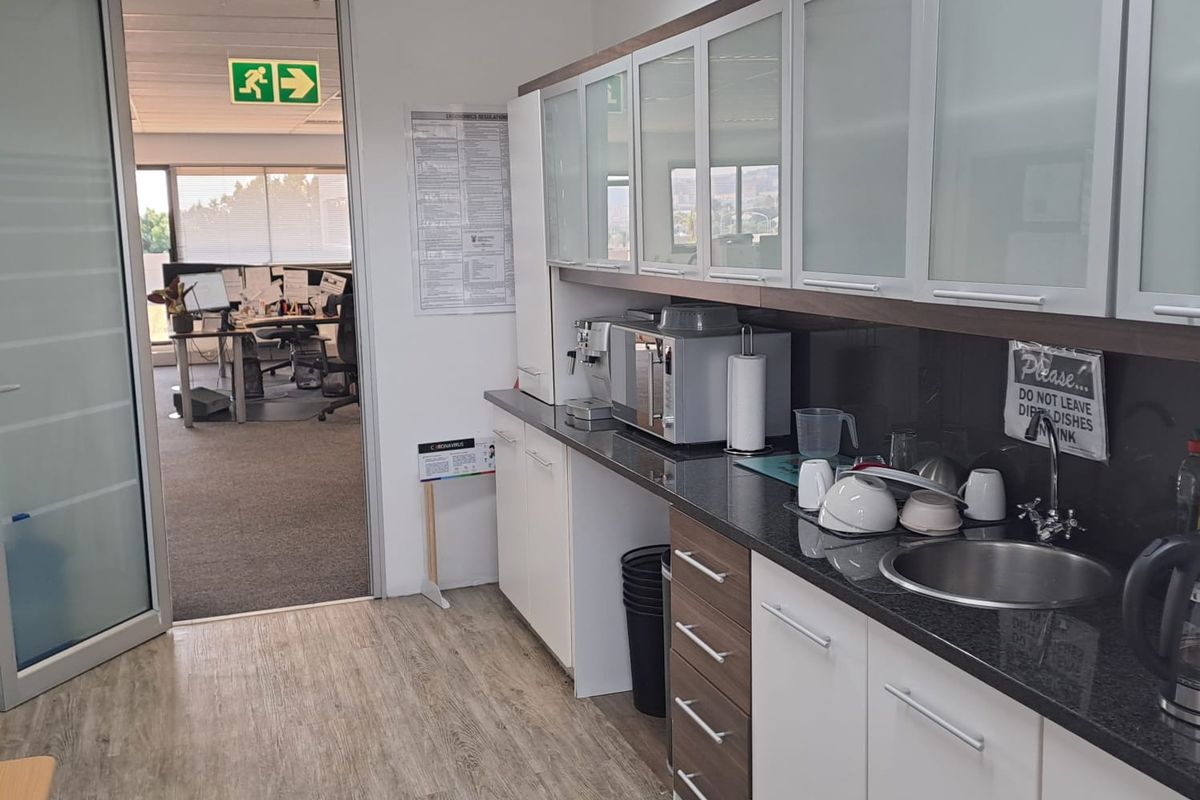 A functional office kitchenette featuring modern cabinetry, granite countertops, a stainless steel sink, and integrated lighting, providing a convenient break area for staff.
