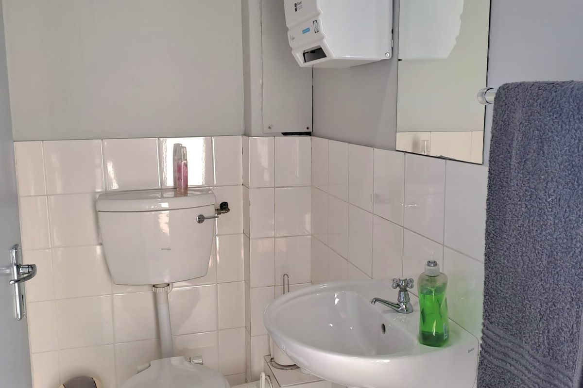 A functional office restroom featuring a wall-mounted basin, standard toilet, and wall-mounted paper towel dispenser with tiled splashbacks.