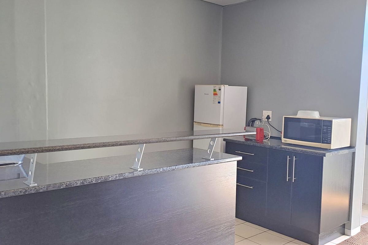 A functional office kitchenette area featuring dark cabinetry, a granite-look countertop, a breakfast bar, and a suspended acoustic ceiling grid.