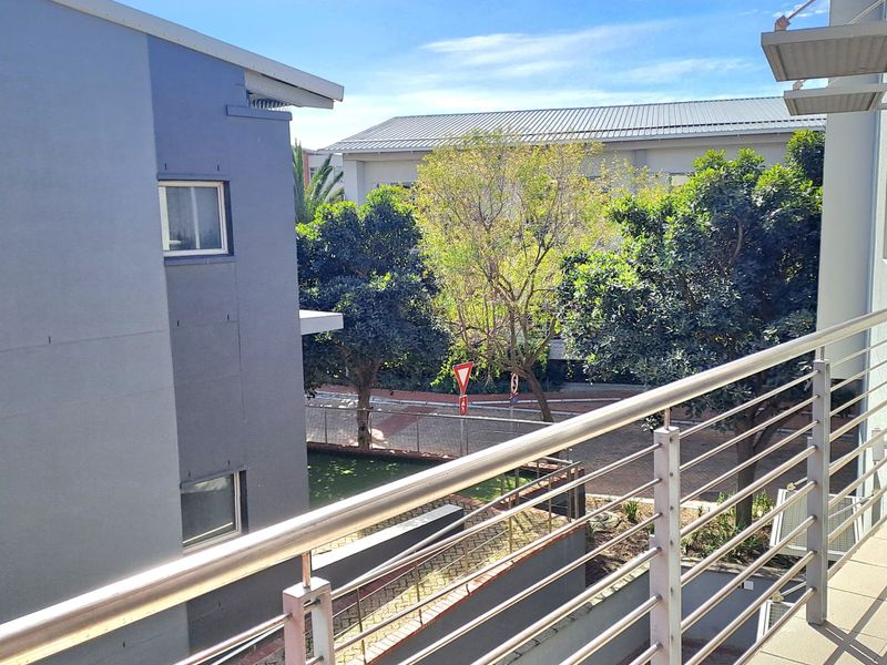 A modern balcony featuring a stainless steel balustrade and tiled flooring, offering an elevated view of the surrounding office complex and landscaped grounds.
