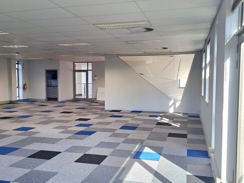 Spacious open-plan office area featuring modern carpet tiles, suspended ceilings with recessed lighting, and a unique geometric glass partition.