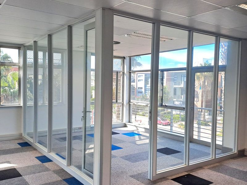 A bright, open-plan office space featuring modern glass partitioning, suspended ceilings, and patterned carpet tiles, offering a professional and versatile work environment.