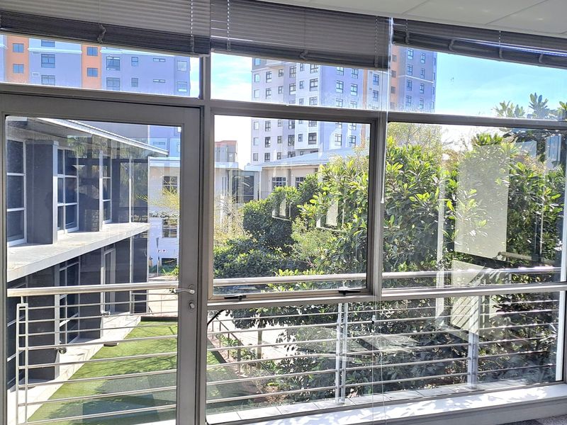 Bright office space featuring large windows, a glass door leading to a balcony with stainless steel railings, and neutral carpet tiles.
