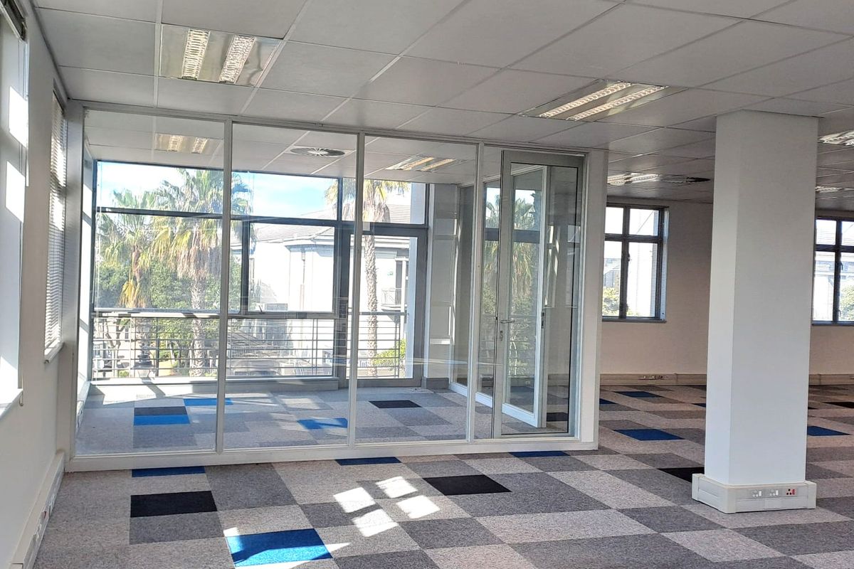 An open-plan office space featuring glass partitioning, suspended ceilings with recessed lighting, and patterned carpet tiles.