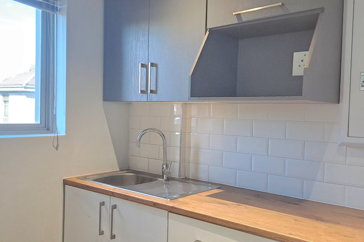 A modern, compact kitchen area featuring clean white cabinetry, a wooden countertop, a stainless steel sink, and a stylish subway tile backsplash.