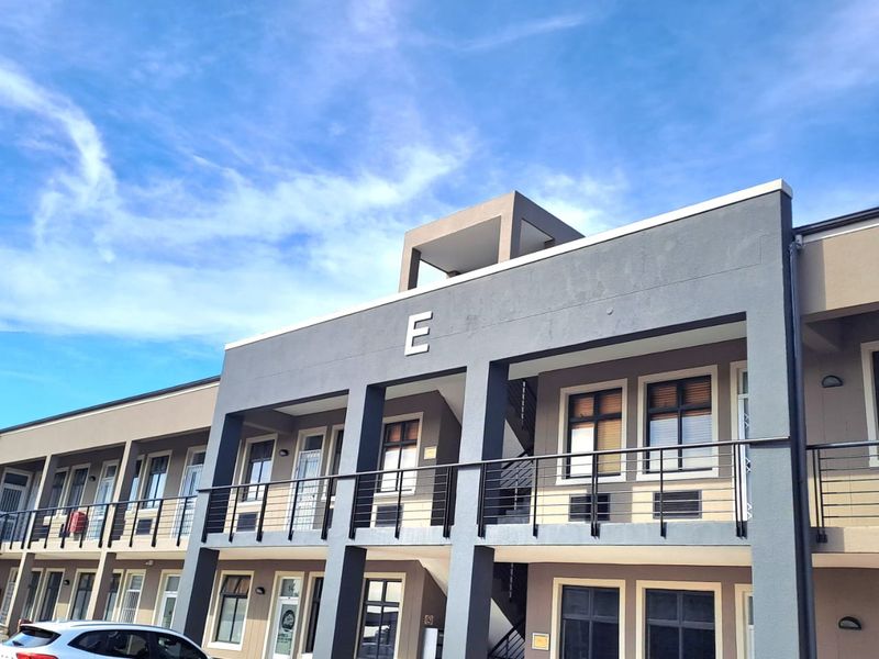 A modern two-story office building facade featuring a grey and beige exterior, balcony access, and designated parking area.
