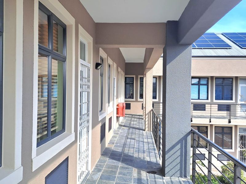 A covered exterior walkway featuring tiled flooring, metal railings, and access to office units with security gates.