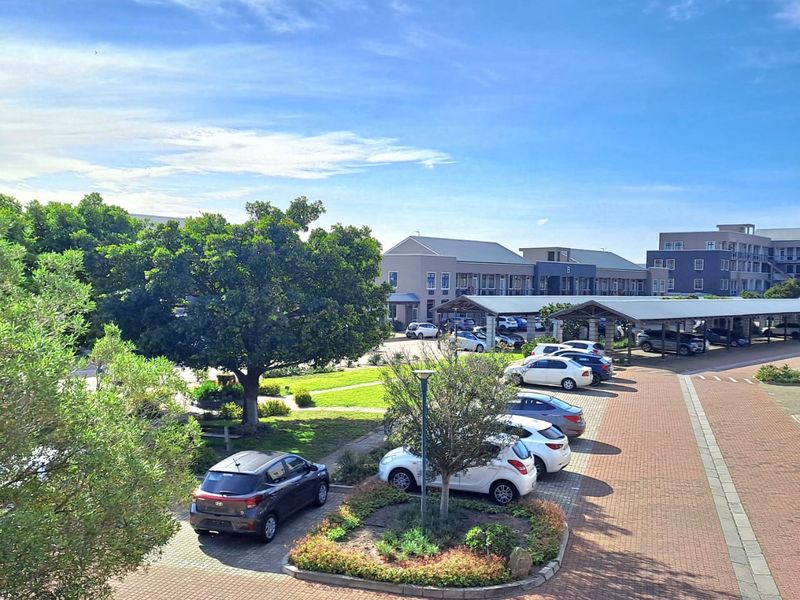 Elevated view of the office park grounds, featuring paved parking areas, covered carports, landscaped garden beds, and mature trees.