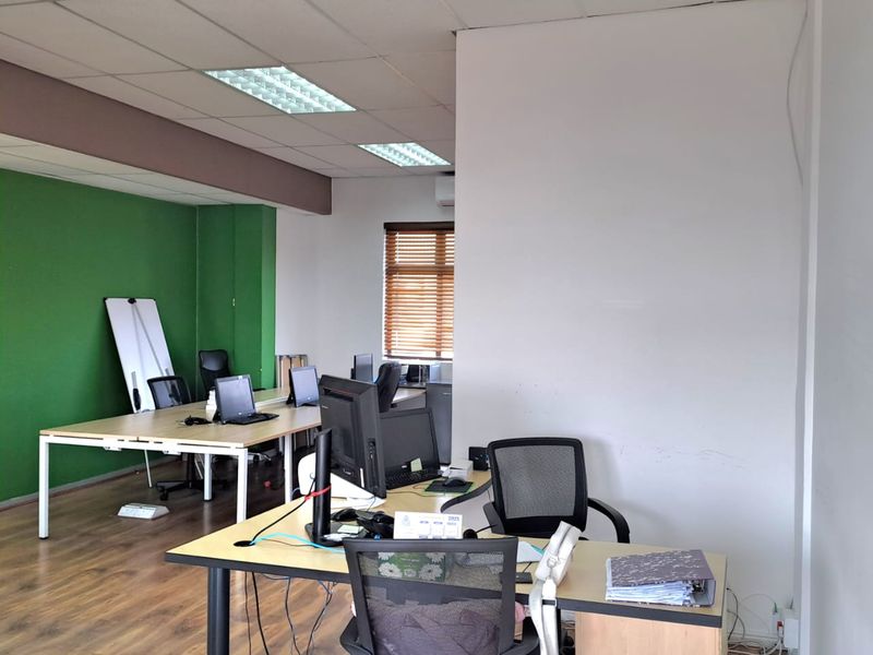 A functional open-plan office space featuring wood-look flooring, recessed ceiling lighting, and a vibrant green accent wall.