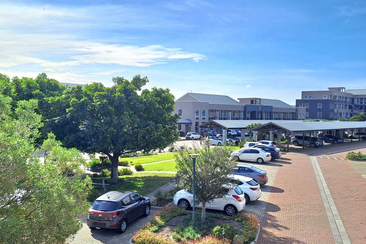 Elevated view of the office park grounds, featuring paved parking areas, covered carports, landscaped garden beds, and mature trees.