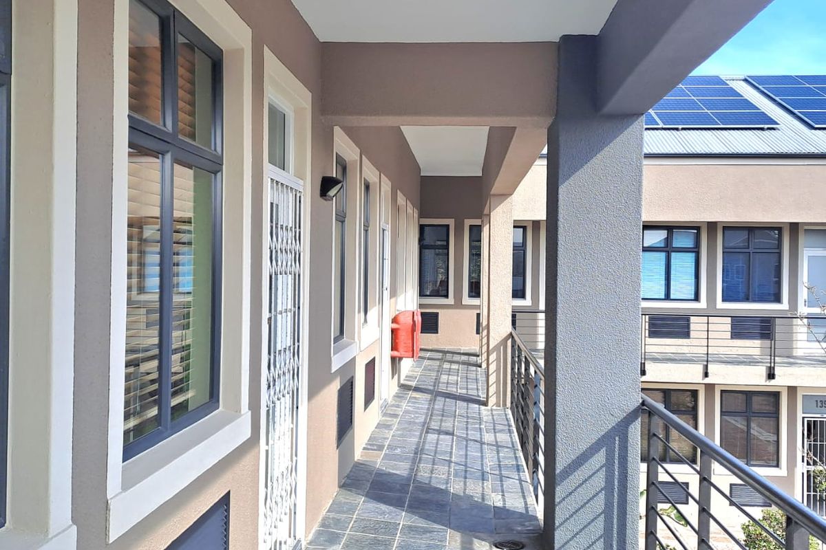 A covered exterior walkway featuring tiled flooring, metal railings, and access to office units with security gates.