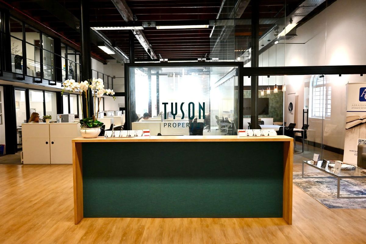 Modern office reception area featuring a custom desk, glass partitioning, and an open-plan layout with exposed industrial-style ceiling beams.