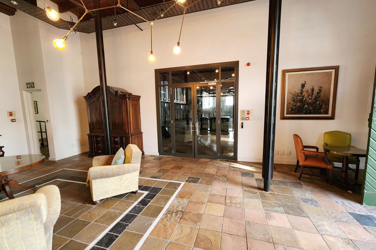 Spacious office reception area featuring high ceilings with exposed timber beams, black structural columns, and durable stone tile flooring with double glass door access.
