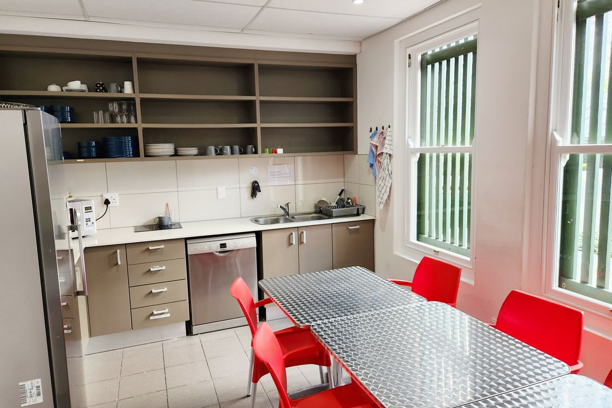 A functional office kitchenette featuring built-in cabinetry, stainless steel sink, tiled backsplash, and integrated dishwasher, providing a practical break area for staff.