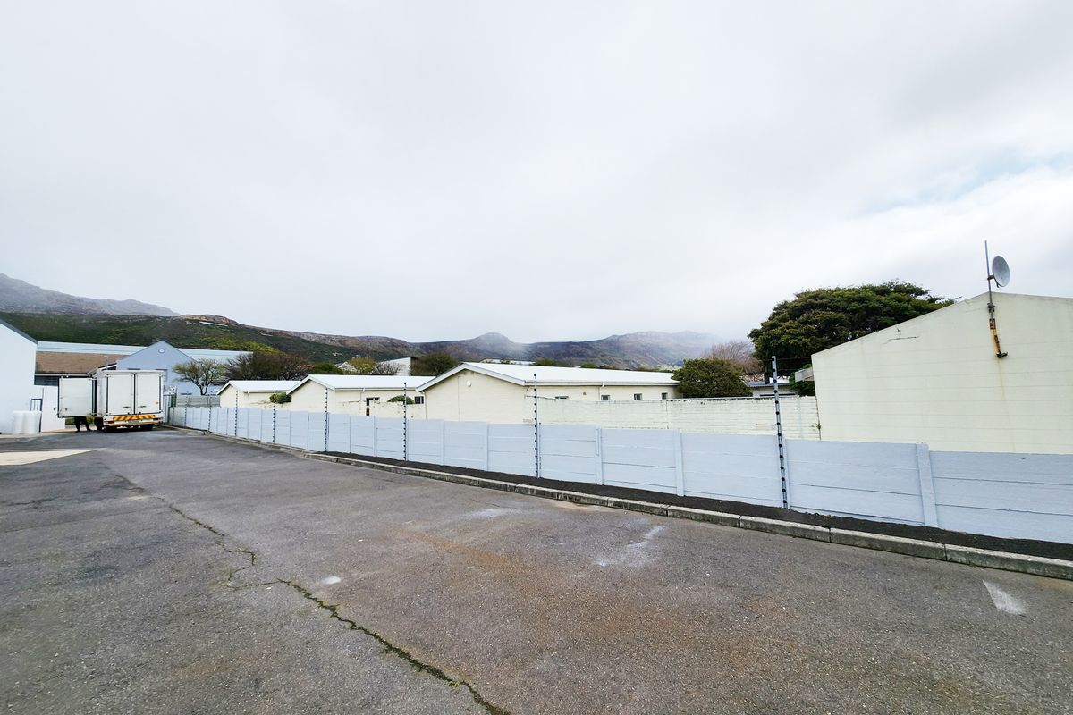 Exterior view of the industrial property featuring a paved yard area, perimeter wall with electric fencing, and surrounding industrial buildings.