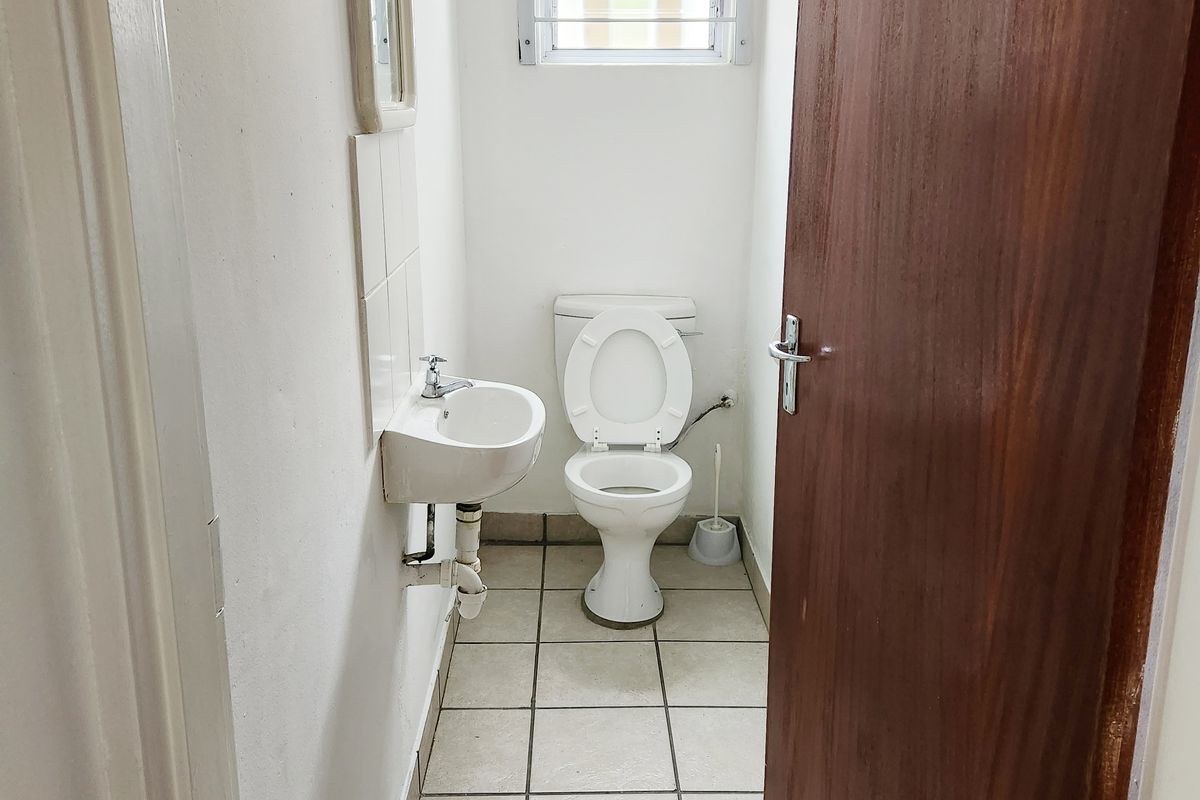 A compact industrial restroom featuring a wall-mounted basin, a standard toilet, and tiled flooring with a small window for ventilation.