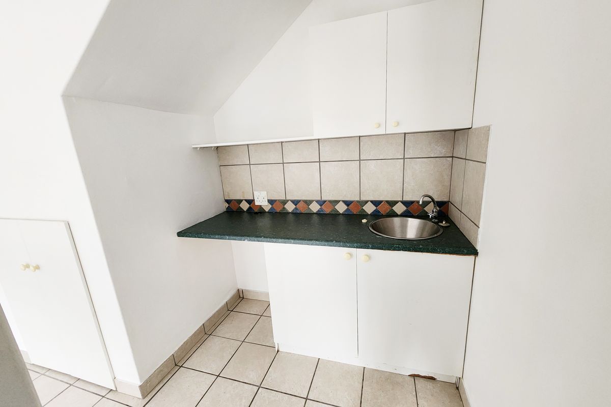 A compact kitchenette area featuring white cabinetry, a dark laminate countertop, a stainless steel sink, and tiled flooring.