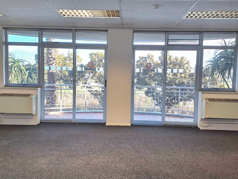 Empty office space featuring carpeted flooring, suspended ceiling with recessed lighting, and large sliding glass doors providing natural light and balcony access.